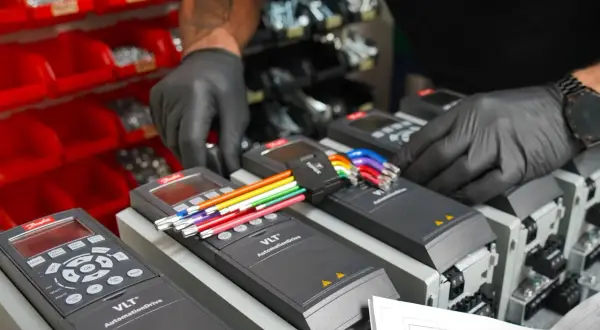 Ręce w czarnych rękawiczkach podłączają kolorowe przewody do falowników VLT AutomationDrive, kluczowych dla sterowania wektorowego.