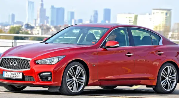 Czerwony infiniti samochód z kierowcą za kierownicą, na tle miejskiej panoramy.