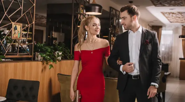 Elegancka para w stylizacjach zgodnych z dress code koktajlowy: kobieta w czerwonej sukni, mężczyzna w garniturze.