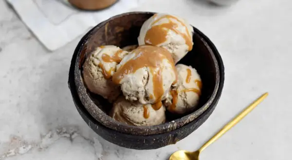 Schüssel mit erdnussbutter eis, beträufelt mit Karamellsauce. Ein goldener Löffel liegt daneben.