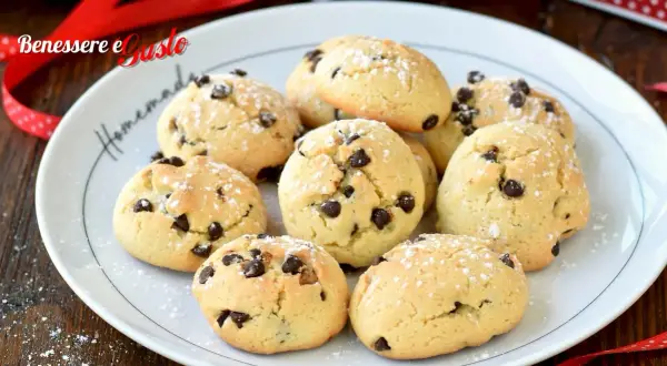 Biscotti con gocce di cioccolato spolverati di zucchero a velo su un piatto bianco, pronti per essere gustati.