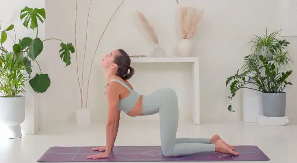 Mujer en postura de la vaca, arqueando la espalda y mirando hacia arriba en una esterilla de yoga.