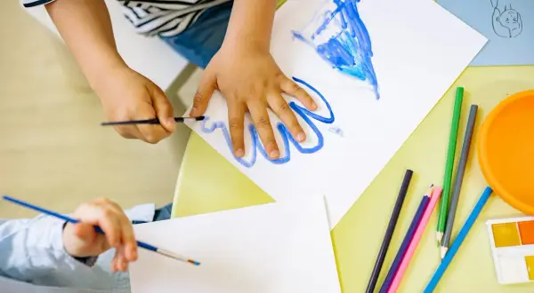 Manos de niños pintando con acuarelas y lápices de colores, aprendiendo los lomloe saberes básicos.