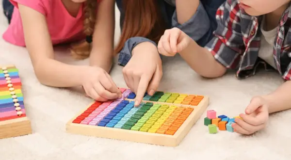 Kinder lernen spielerisch Mathematik im Kindergarten mit bunten Holzbausteinen und einer Multiplikationstafel.