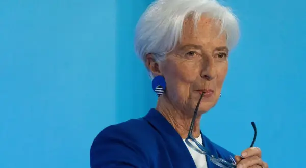 Christine Lagarde mit Brille im Mund, nachdenklich vor dem Hintergrund des EZB-Zinsentscheids.