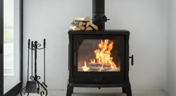 Ein brennender Holzofen mit Holzscheiten und einem Fächer zur Steigerung des holzofen wirkungsgrad. Daneben ein Kaminbesteck.