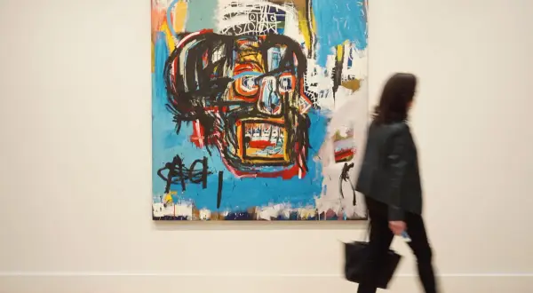 A woman walks past a vibrant, abstract painting, a striking example of Basquiat's famous paintings, featuring a bold, stylized face.