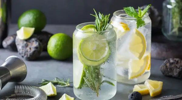 Orzeźwiający drink z ginem, limonką i rozmarynem, obok cytryny i mięty. Idealny na letnie popołudnie.