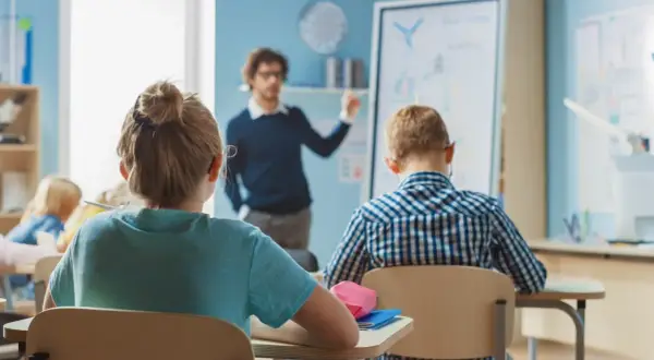 Nauczyciel tłumaczy lekcję, a uczniowie siedzą w ławkach. Czy wysokie zarobki nauczycieli wpłyną na jakość edukacji?