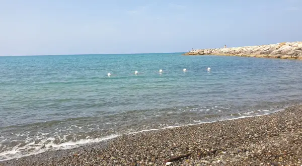 Spiagge più belle della Marina di Cecina: mare azzurro, ciottoli levigati e un molo roccioso con qualche bagnante.