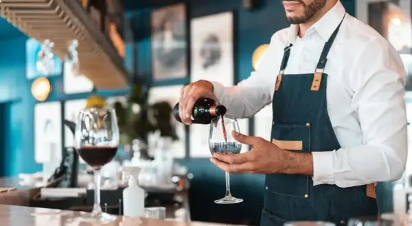 Doświadczony sommelier wina nalewa czerwone wino do kieliszka w eleganckiej restauracji.