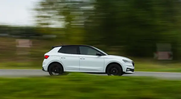 Un Skoda Fabia 130 blanco con techo negro se mueve rápido por una carretera rural, con el paisaje difuminado por la velocidad.