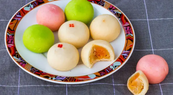 Kolorowe mochi z żółtym nadzieniem na talerzu z ozdobnym brzegiem.