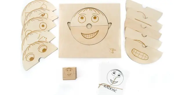 Drewniane pomoce dydaktyczne do nauki emocji: puzzle twarzy, kostka i karty z buźkami.