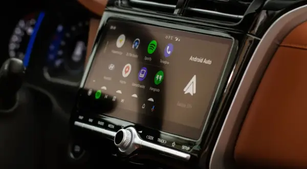 Ekran multimedialny z Android Auto, pokazujący ikony aplikacji: Spotify, Telefon, Mapy. W tle widać fragment deski rozdzielczej.