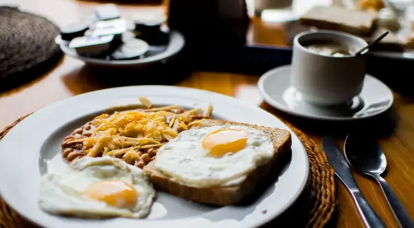 Un petit déjeuner sportif : œufs au plat, haricots et fromage râpé sur une assiette, avec une tasse de café à côté.
