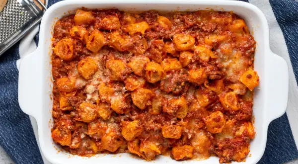 Tortelli ripieni di carne al forno, ricoperti di sugo rosso e formaggio fuso, pronti per essere gustati.