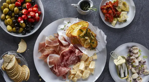 Plateau de charcuterie, fromages, olives, tomates séchées, artichauts, toasts à l'ail et sardines. Une recette antipasti italien facile pour un apéritif gourmand.
