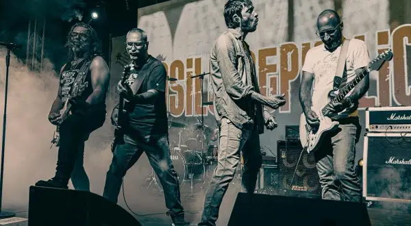La band "Asilo Republic" sul palco, con chitarristi e cantante in azione, avvolti dal fumo.