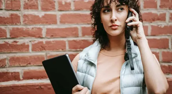 Kobieta rozmawia przez telefon, trzymając tablet. Dyskutuje, czy pracodawca może odmówić urlopu na żądanie.