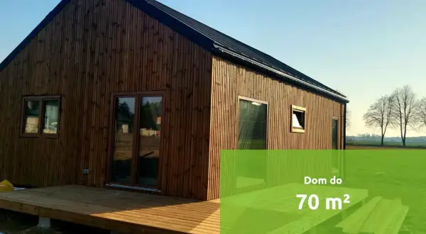 Drewniany budynek gospodarczy z tarasem, w tle pole i drzewa. Idealny na mały dom do 70 m².