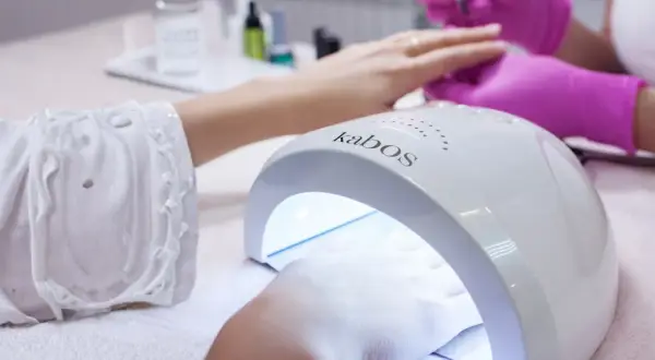 Dłoń w lampie UV do paznokci. Zastanawiasz się, ile trzymać bazę w lampie? Czas utwardzania zależy od produktu.