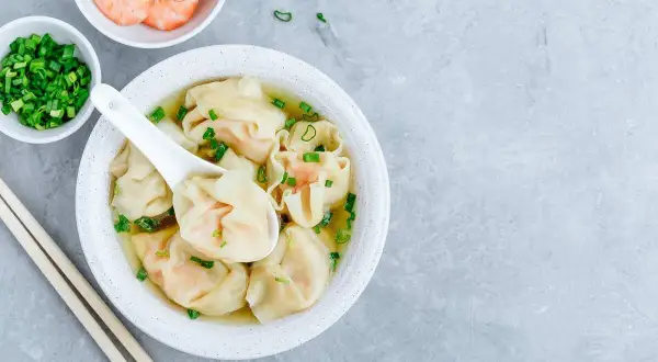 Aksamitna zupa wonton z krewetkami i szczypiorkiem, podana z pałeczkami.