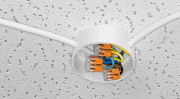 Nowe złącza WAGO ułatwiają wymianę instalacji elektrycznej. Biała puszka sufitowa z kolorowymi przewodami i pomarańczowymi zaciskami.