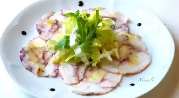 Delicato carpaccio di polpo, affettato sottile e condito con olio e limone, guarnito con insalata fresca e gocce di aceto balsamico.