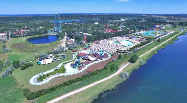 Mirabilandia, un parco acquatico con scivoli colorati e piscine, si trova vicino a un lago, con una ruota panoramica sullo sfondo.
