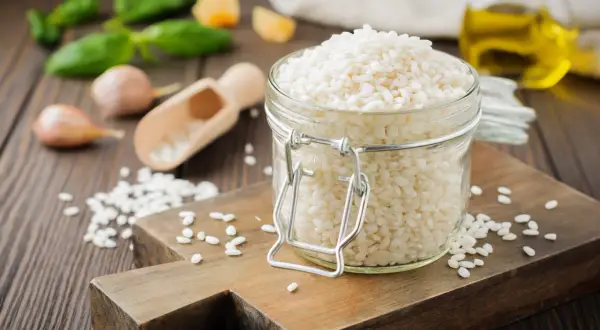 Słoik z ryżem do risotto, obok czosnek, bazylia i oliwa.