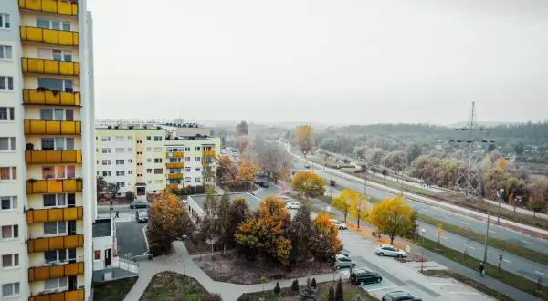 Widok na osiedle z blokami mieszkalnymi i drogą. Jesienne drzewa dodają koloru. Czy mieszkania potanieją?