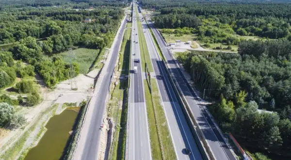 Szeroka autostrada S7 Warszawa-Grójec, otoczona lasami, z kilkoma samochodami w ruchu.