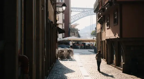 A lone figure walks down a sun-drenched cobblestone street in a European city, a perfect scene for street photography.