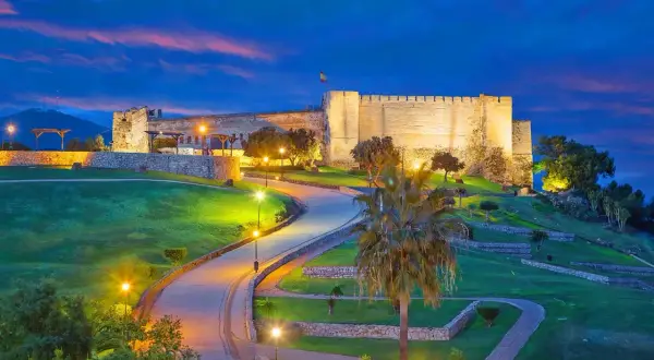 Castillo Sohail iluminado al atardecer, un lugar imprescindible que ver en Fuengirola. Caminos serpenteantes y palmeras bajo un cielo azul intenso.