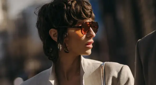 Frau mit einem frechen Pixie Cut, Sonnenbrille und Blazer.