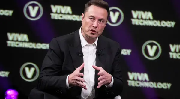 Elon Musk w garniturze, przemawiający na tle logo Viva Technology.