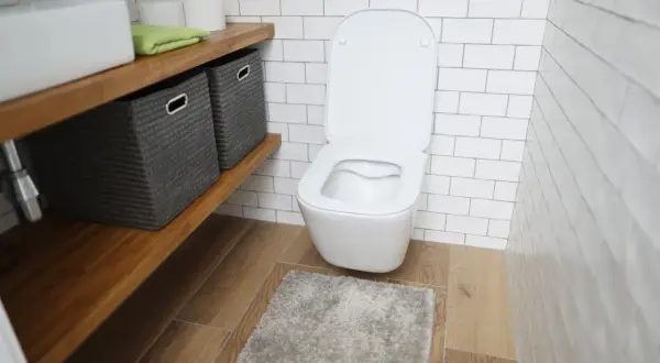 Nowoczesna łazienka z podwieszanym WC. Obok półka z koszami, ręcznikiem i papierem toaletowym. Widać, ile miejsca na wc podwieszane zajmuje.