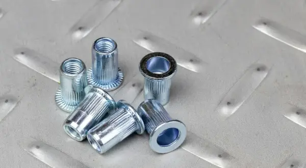 Kilka metalowych nitonakrętek leży na chropowatej, metalowej powierzchni.