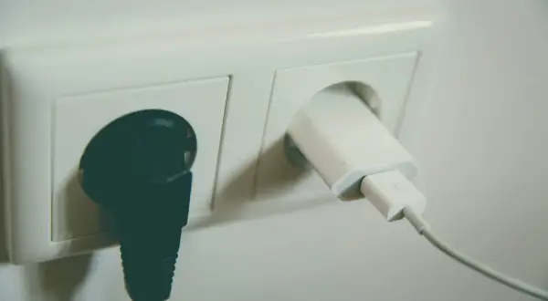 Dwa gniazdka elektryczne. W jednym czarna wtyczka, w drugim biała ładowarka z kablem. Napięcie w gniazdku zasila urządzenia.