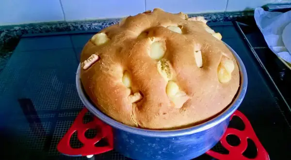 A golden-brown, round bread with chunks of white cheese baked into the top, in a blue baking pan.