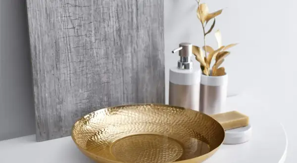 Un bol texturé doré, un distributeur de savon et une barre de savon sur un comptoir blanc, évoquant une ambiance de douche dorée.