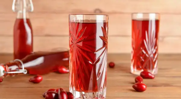 Szklanka z nalewką z derenia, obok butelki i owoców. Idealny przepis na domową nalewkę z derenia.