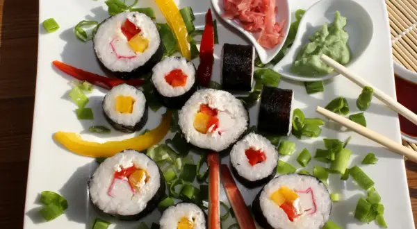 Kolorowe rolki sushi z surimi, papryką i szczypiorkiem, podane z wasabi i imbirem.