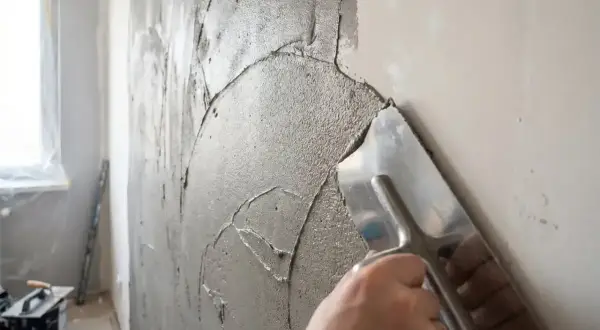 Ręka z kielnią rozprowadza gładką masę gipsową na ścianie, przygotowując ją do malowania.