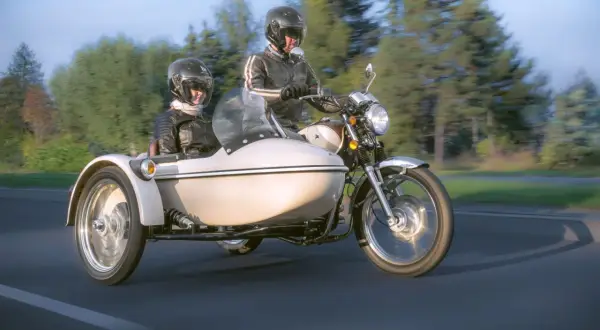 Para podróżuje motocyklem z koszem, ciesząc się jazdą po malowniczej drodze.