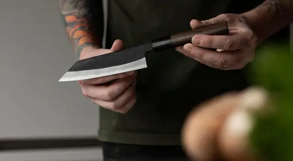 Manos sostienen un cuchillo de chef con hoja de acero VG10, listo para cortar.
