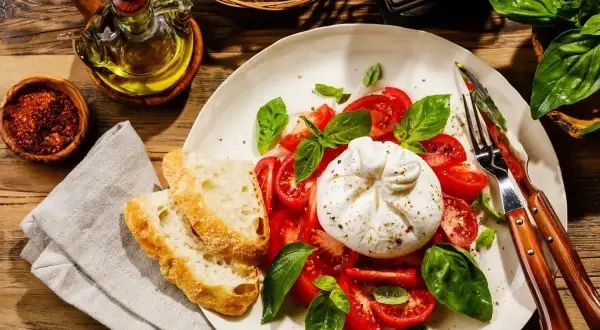 Ser burrata z pomidorami i bazylią, podany z chrupiącym pieczywem. Idealny pomysł na to, ser burrata z czym jeść.