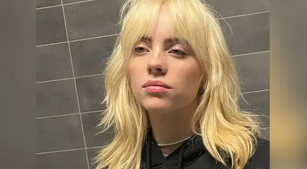 Blond włosy w stylu wolf cut, z grzywką i warstwami, opadające na ramiona.