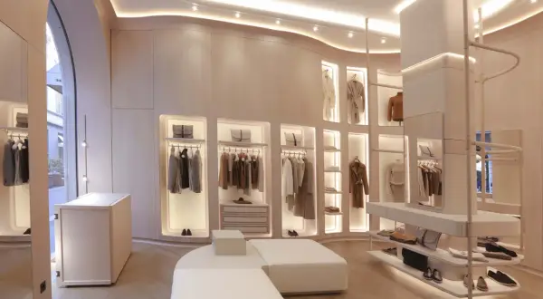 Interni negozio di abbigliamento con abiti eleganti appesi, borse e scarpe in esposizione. L'ambiente è moderno e luminoso, con un design minimalista e finiture in legno chiaro.